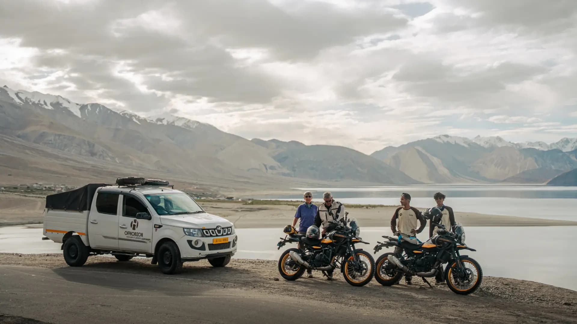 Offhorizon support pickup and four riders with Royal Enfield Himalayan 450 motorcycles on the shore of Pangong Lake in Ladakh